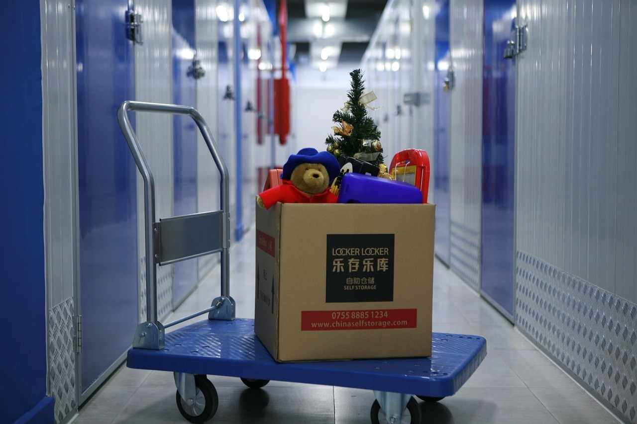 Box with teddy bear and Christmas tree on a dolly inside a self-storage facility hallway with storage units.