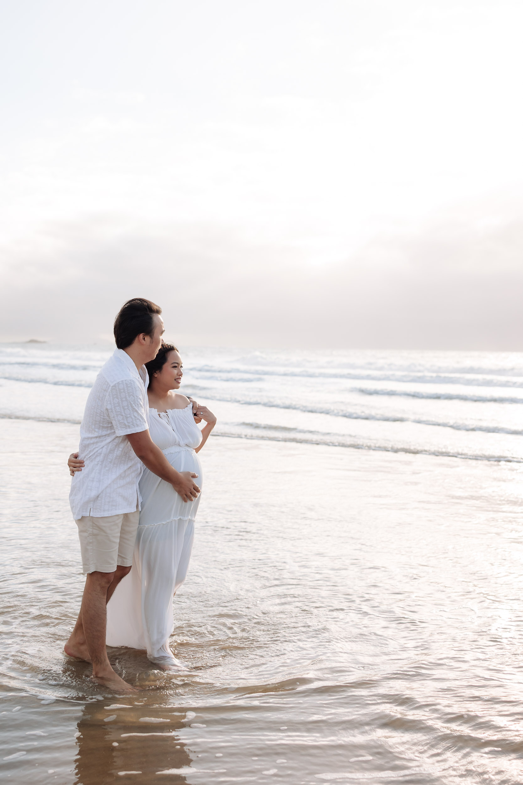Husband touching wife's baby bump standing in the ocean