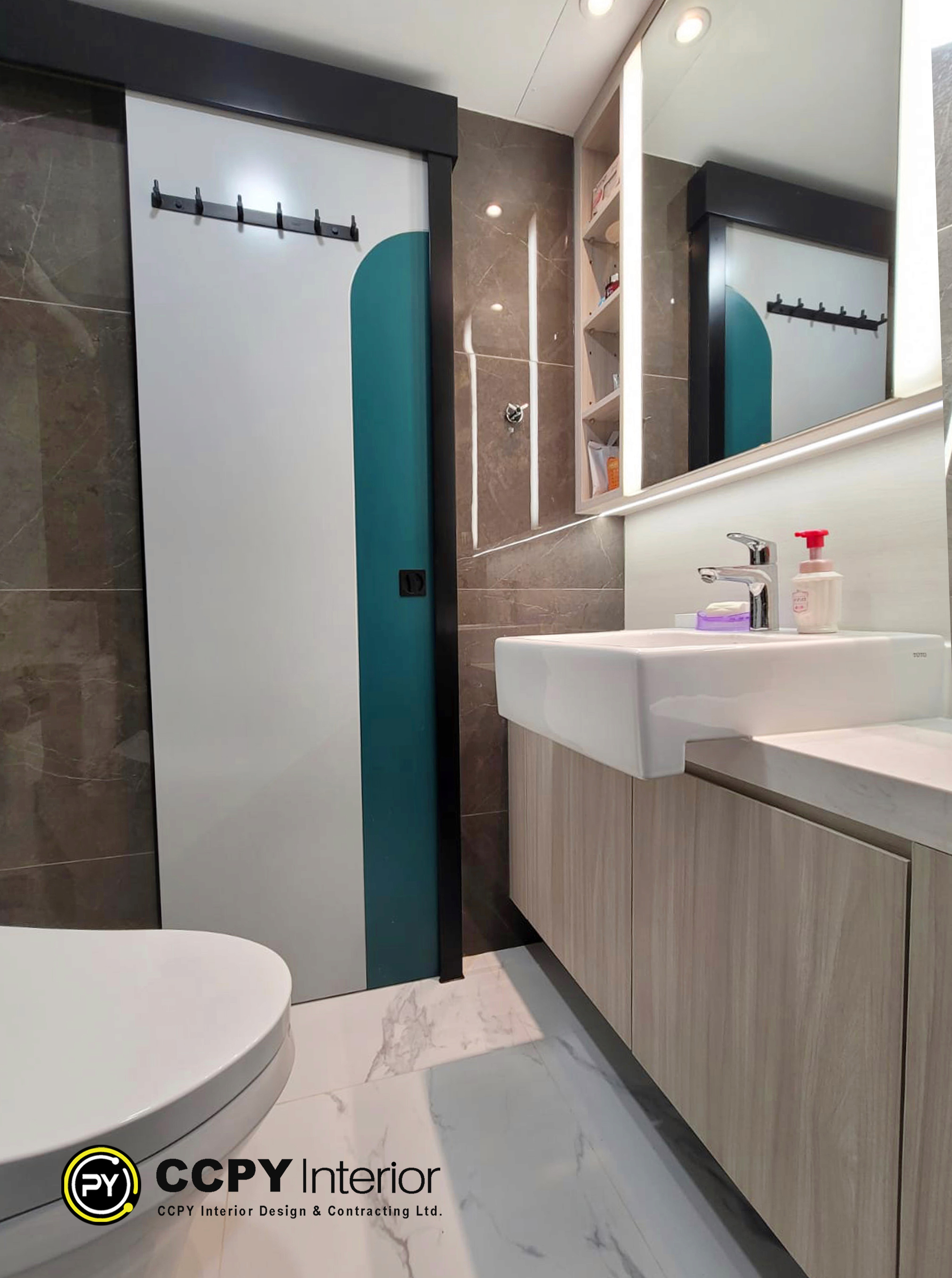 This modern bathroom features a sleek wall-mounted sink and tiled walls.The design includes a contrast between light wood-toned cabinetry and dark grey tiled walls.It utilizes a bright teal accent wall to add a pop of color to the space.The vanity area is completed with a minimalist basin and integrated mirror lighting.
