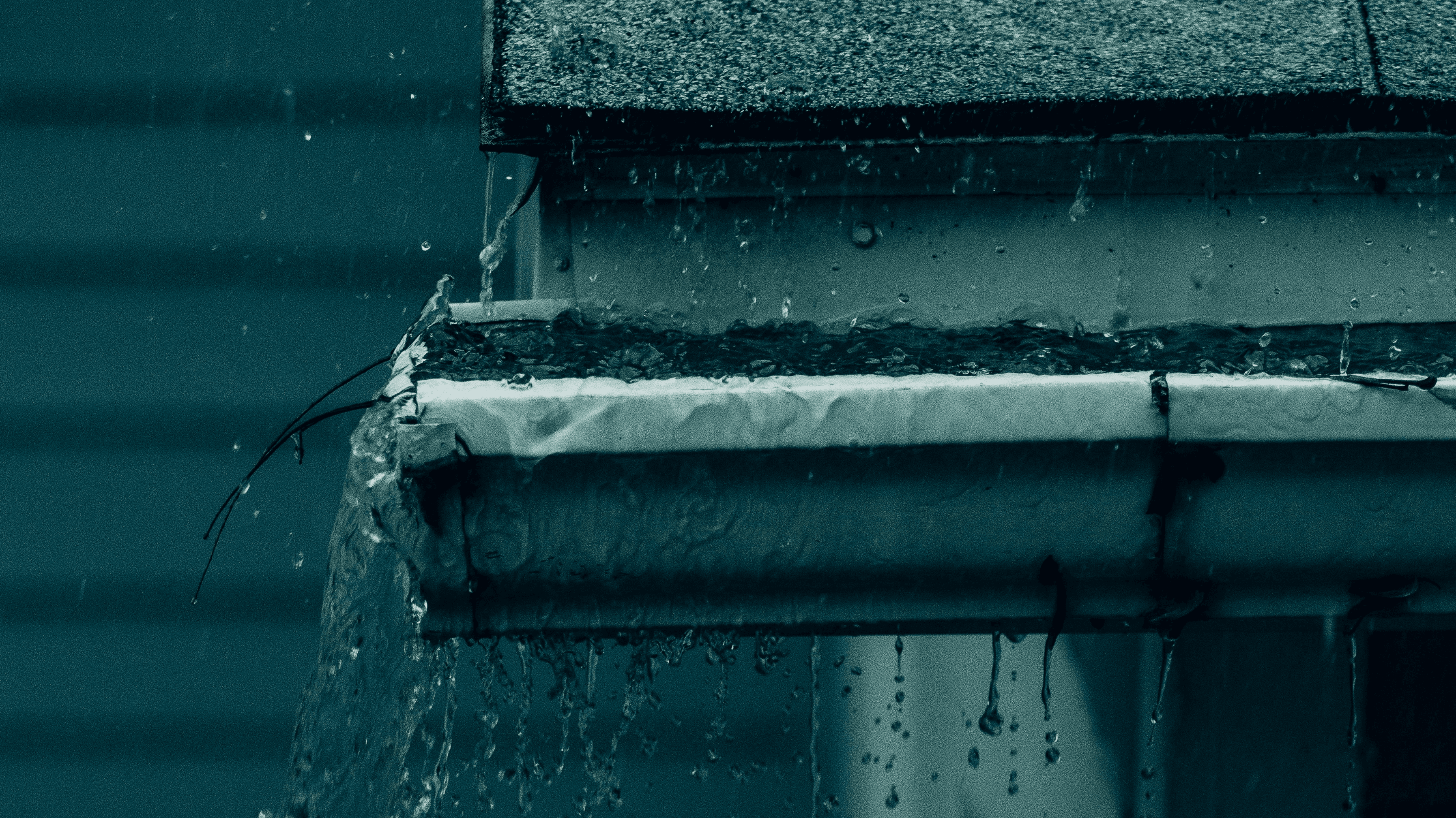 Rain overflows from a rain gutter during an Oklahoma storm on a dark spring day