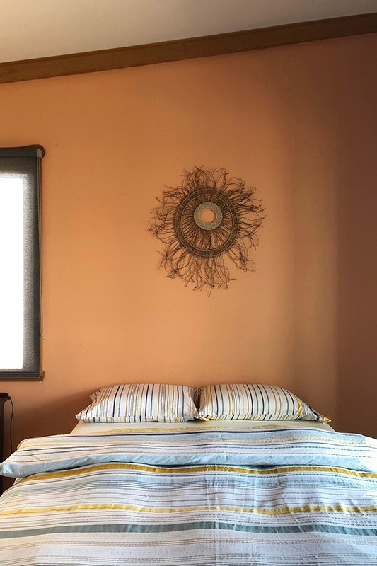 The second bedroom with an apricot wall, striped bedding and a woven sunburst wall piece