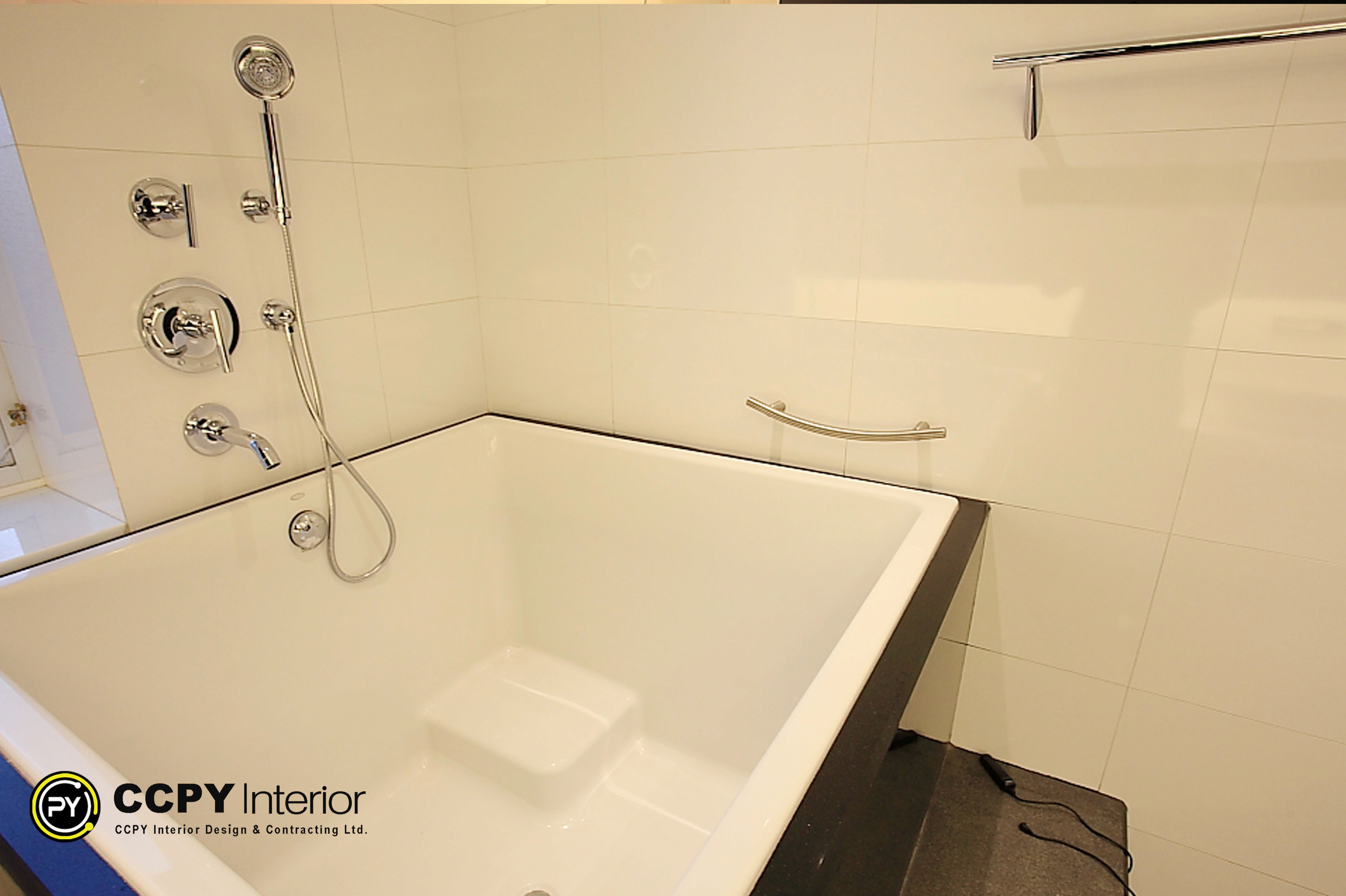 Deep soaking tub in a luxury mansion Perkins Road with chrome handheld shower and minimalist white tile walls.