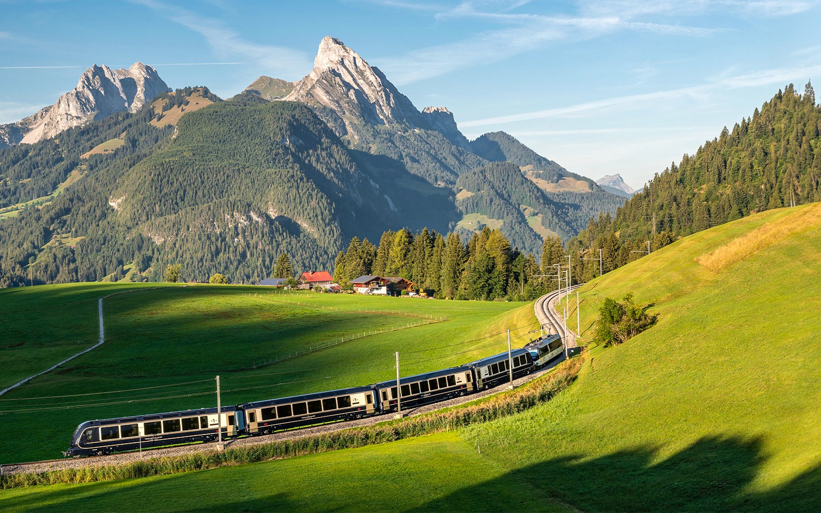 GoldenPass Express train traveling through lush green hills with Interlaken mountains in the background.