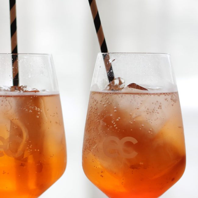 Two orange cocktails with straws in Eclat branded glasses