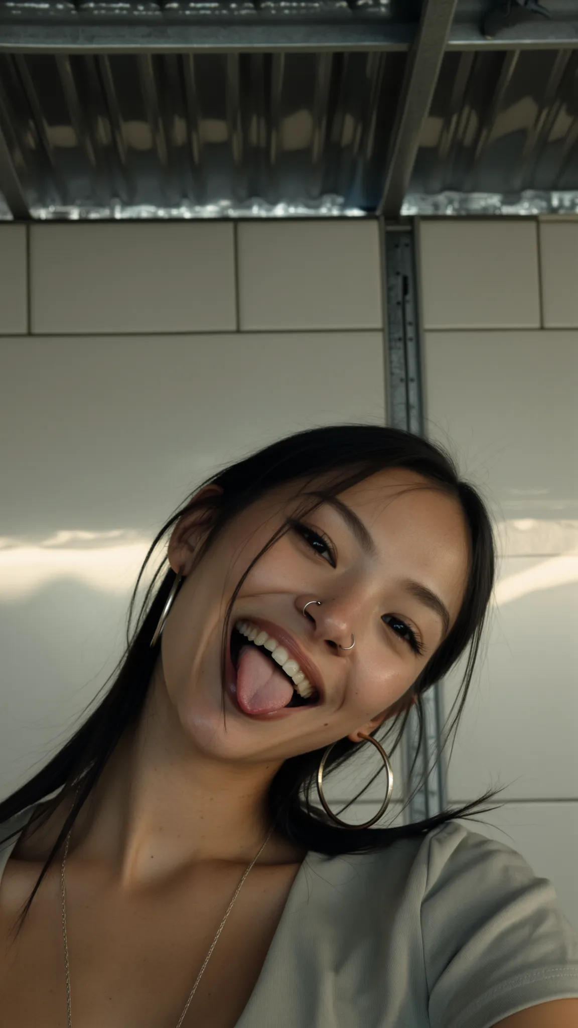 „KI-Model lächelt in Nahaufnahme und streckt spielerisch die Zunge raus; moderner, urbaner Selfie-Look mit großen Creolen und Nasenpiercing.