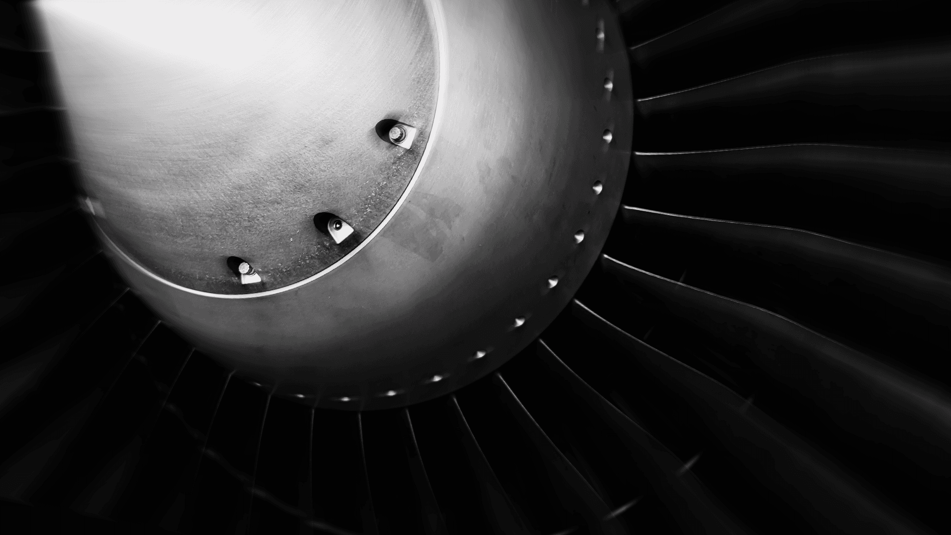 Black and white close-up of a jet engine turbine, with radial blades and metallic surface details under dramatic lighting.