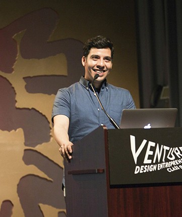 portrait of a young man with a blue shirt giving a speech from the stand