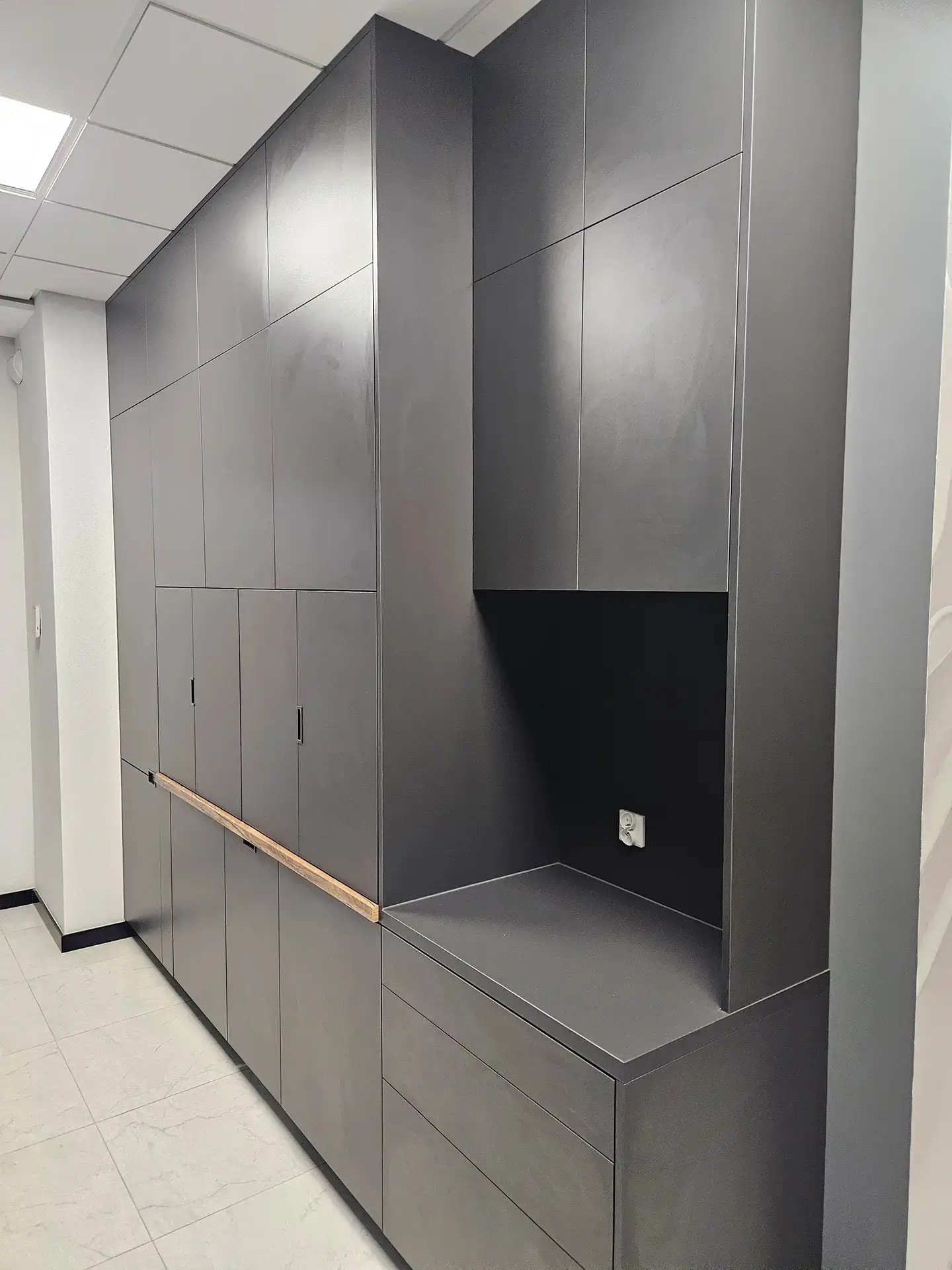 Wysoka zabudowa szafowa do biura w kolorze antracytowym z funkcjonalną wnęką serwisową.