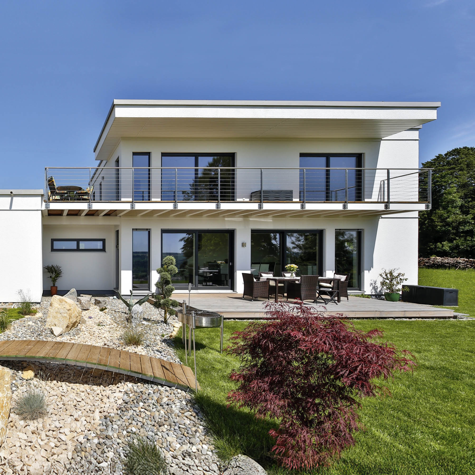 Moderne weiße Villa mit großem Balkon, Glasfronten, Terrasse mit Sitzmöbeln und Garten mit Zierteich sowie roten Ahorn.