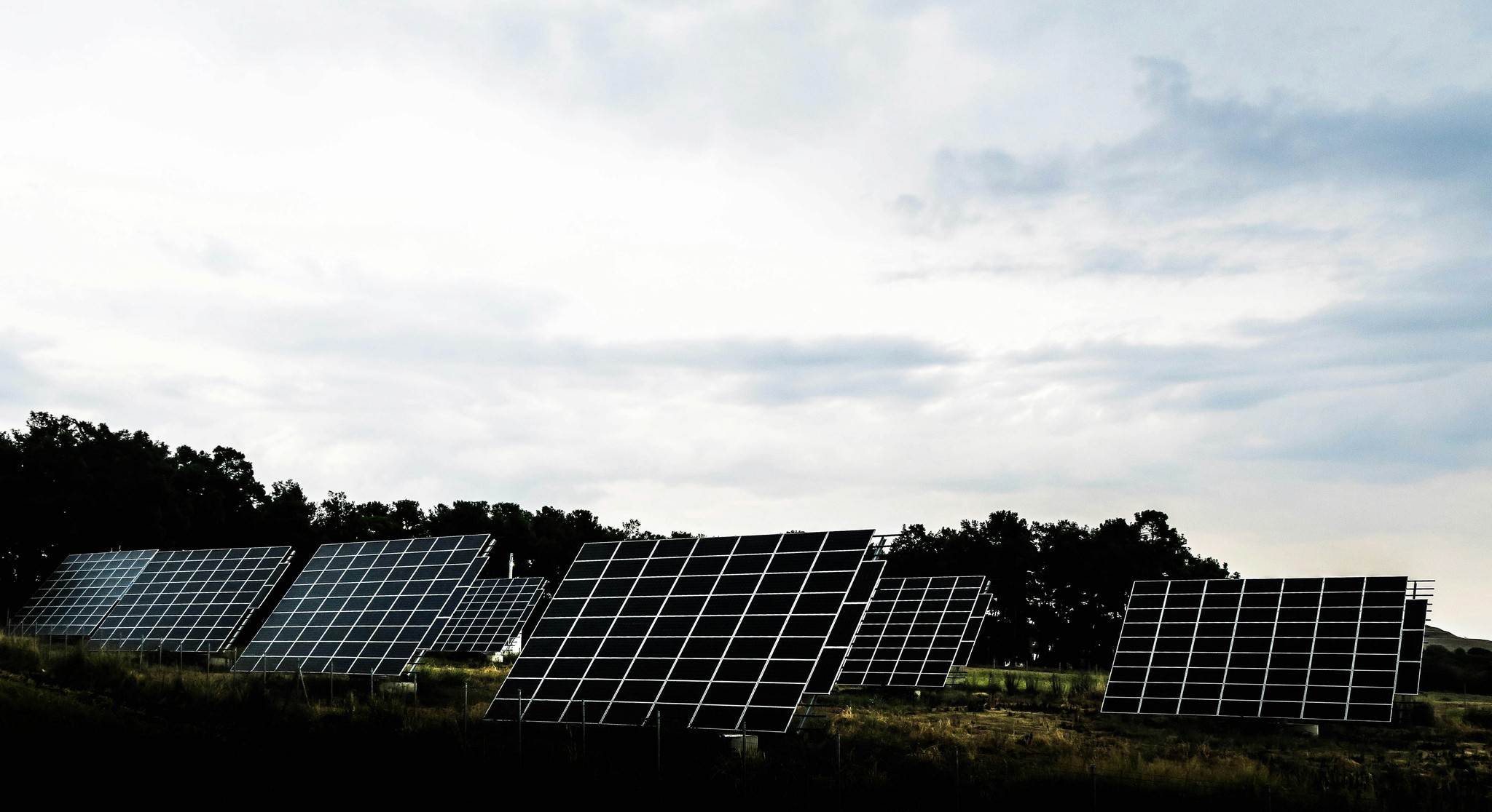 Solar panels arranged in a field under a cloudy sky, generating renewable energy. 