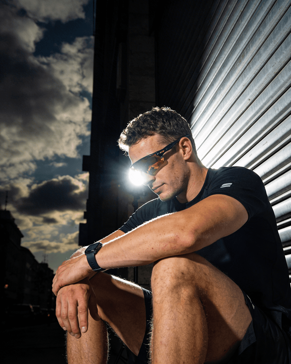 A man in athletic gear and sunglasses sitting against a shutter.