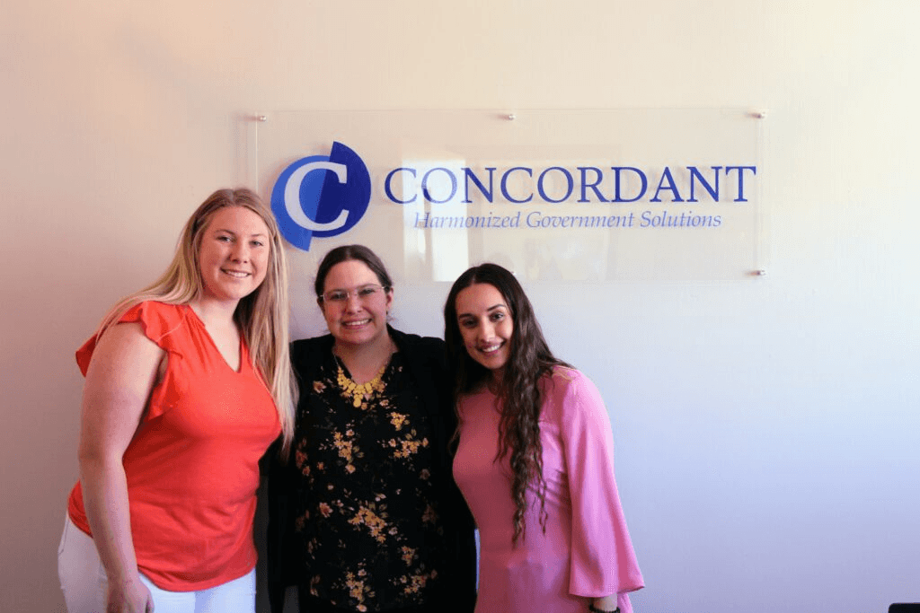 Three members of the Concordant team in front of the Concordant logo