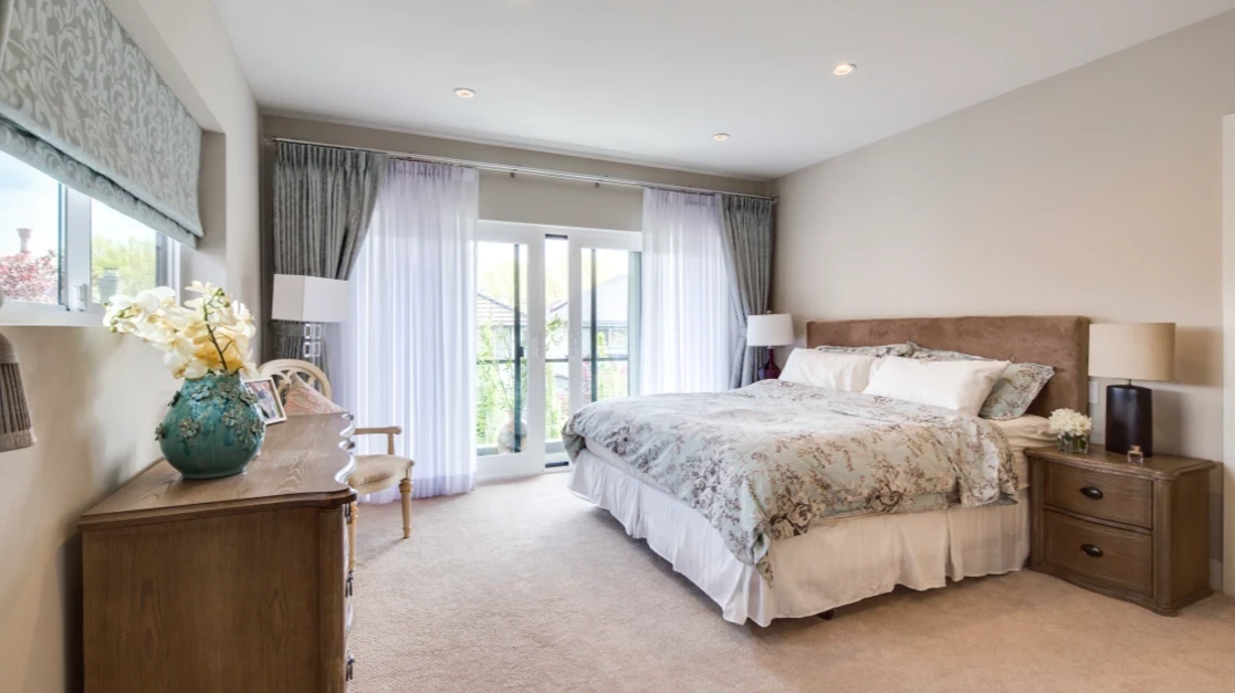 Master bedroom with upholstered headboard, French doors opening to private balcony, elegant window treatments, and plush carpeting in Richmond custom home
