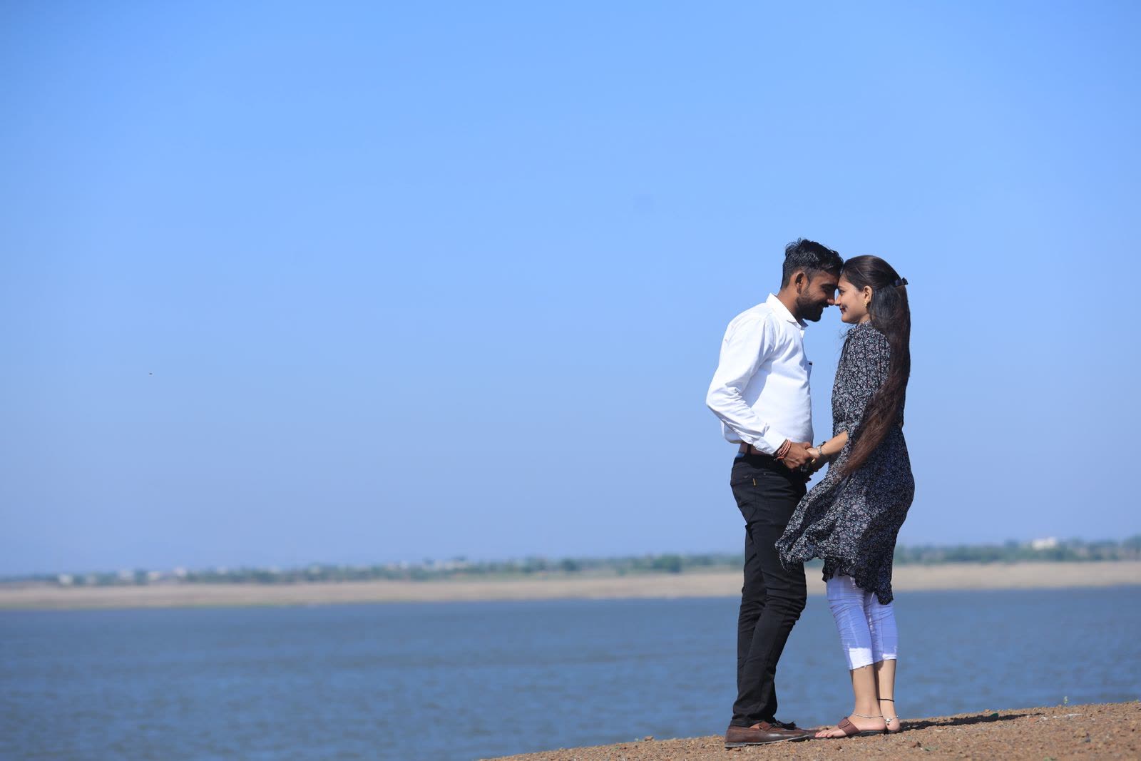 Couple standing close at the edge of a lake with a flat far shore behind them