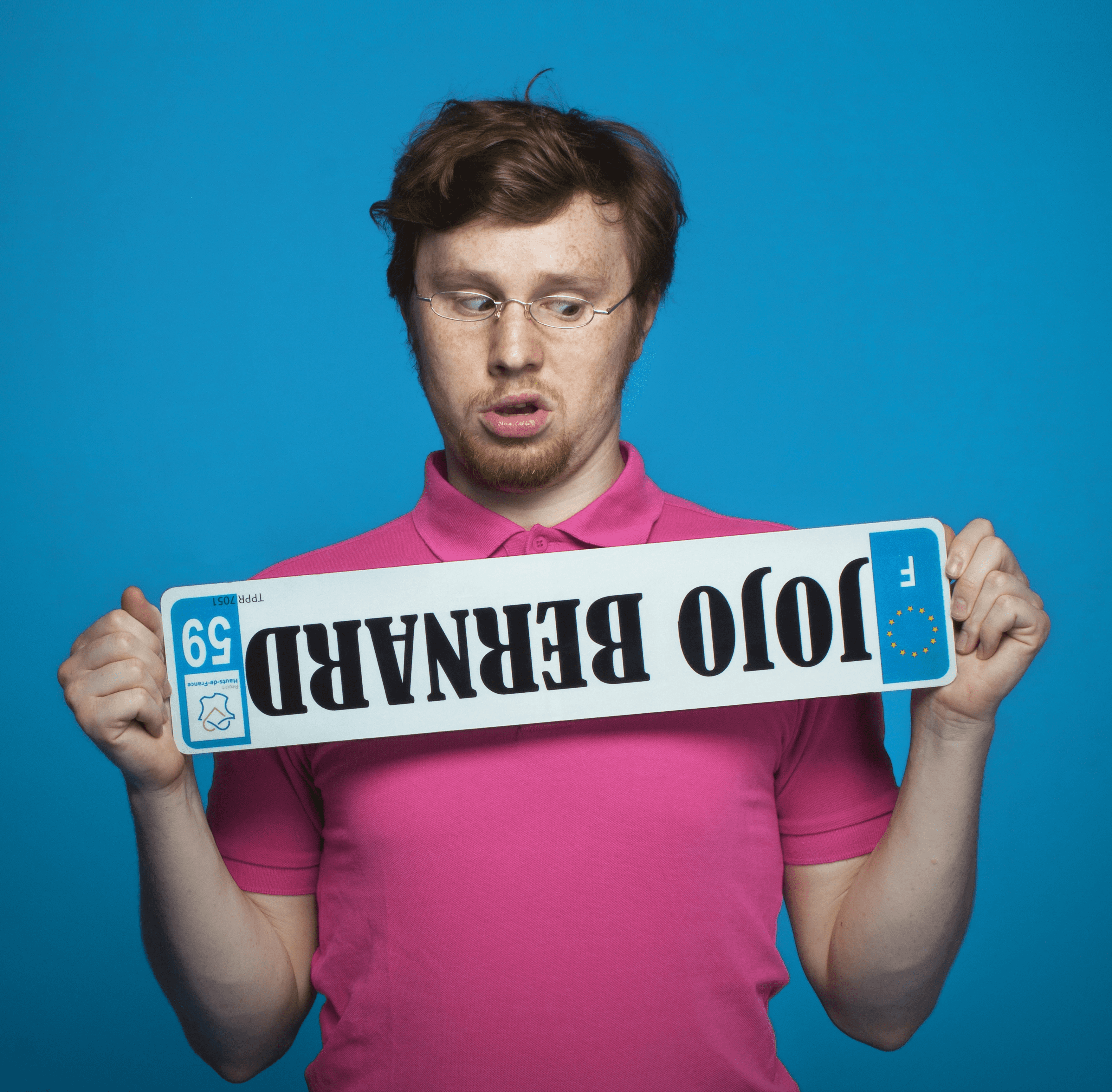 A man with wavy brown hair smiles slightly while wearing a black turtleneck and blazer. The background is softly blurred, suggesting a sunny outdoor setting.