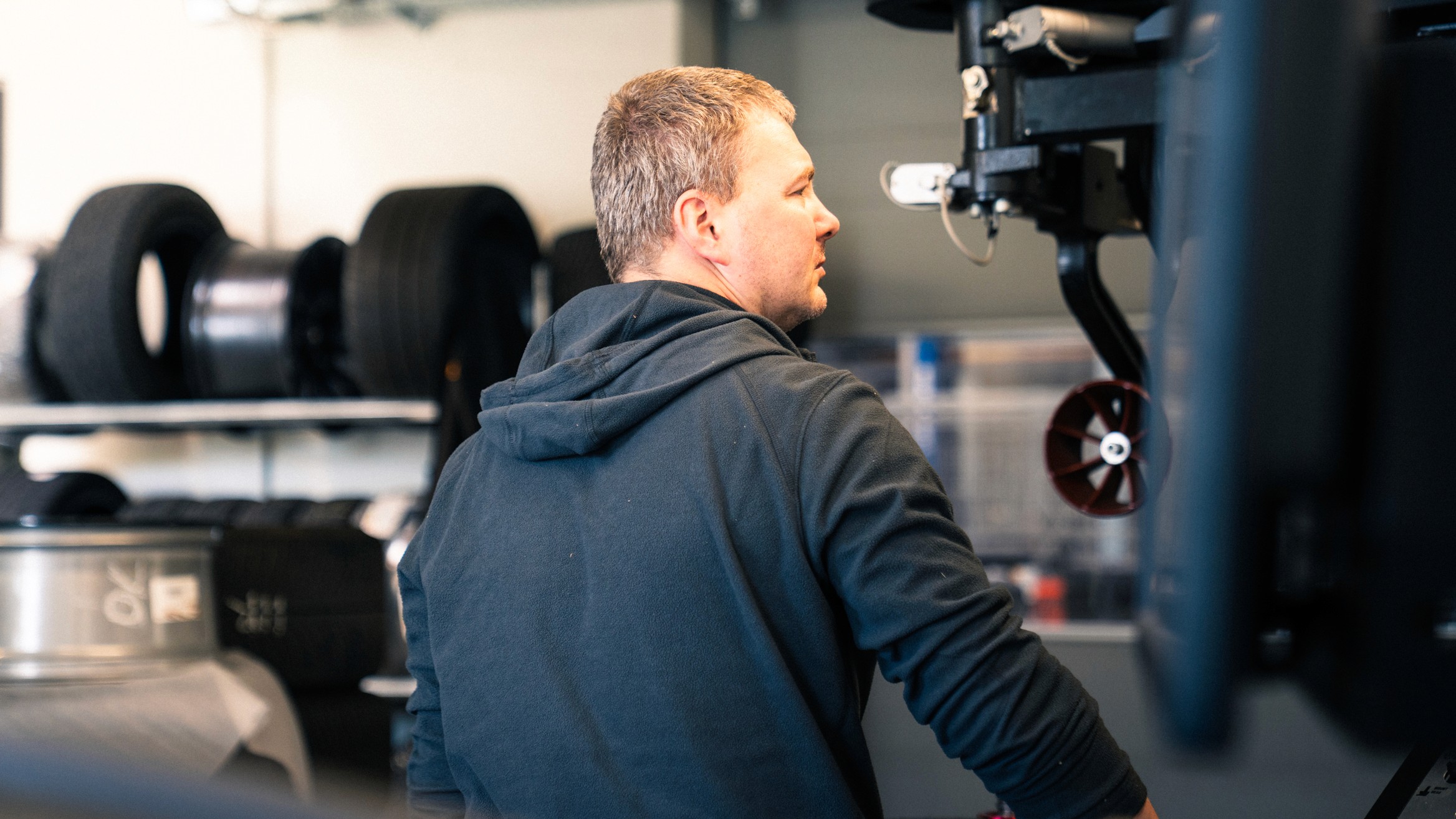 Schwarz-weiß Foto eines Mitarbeiters in der Werkstatt von Insiderfelgen, konzentriert bei der Arbeit an einer Maschine – symbolisiert Fachwissen und Engagement.