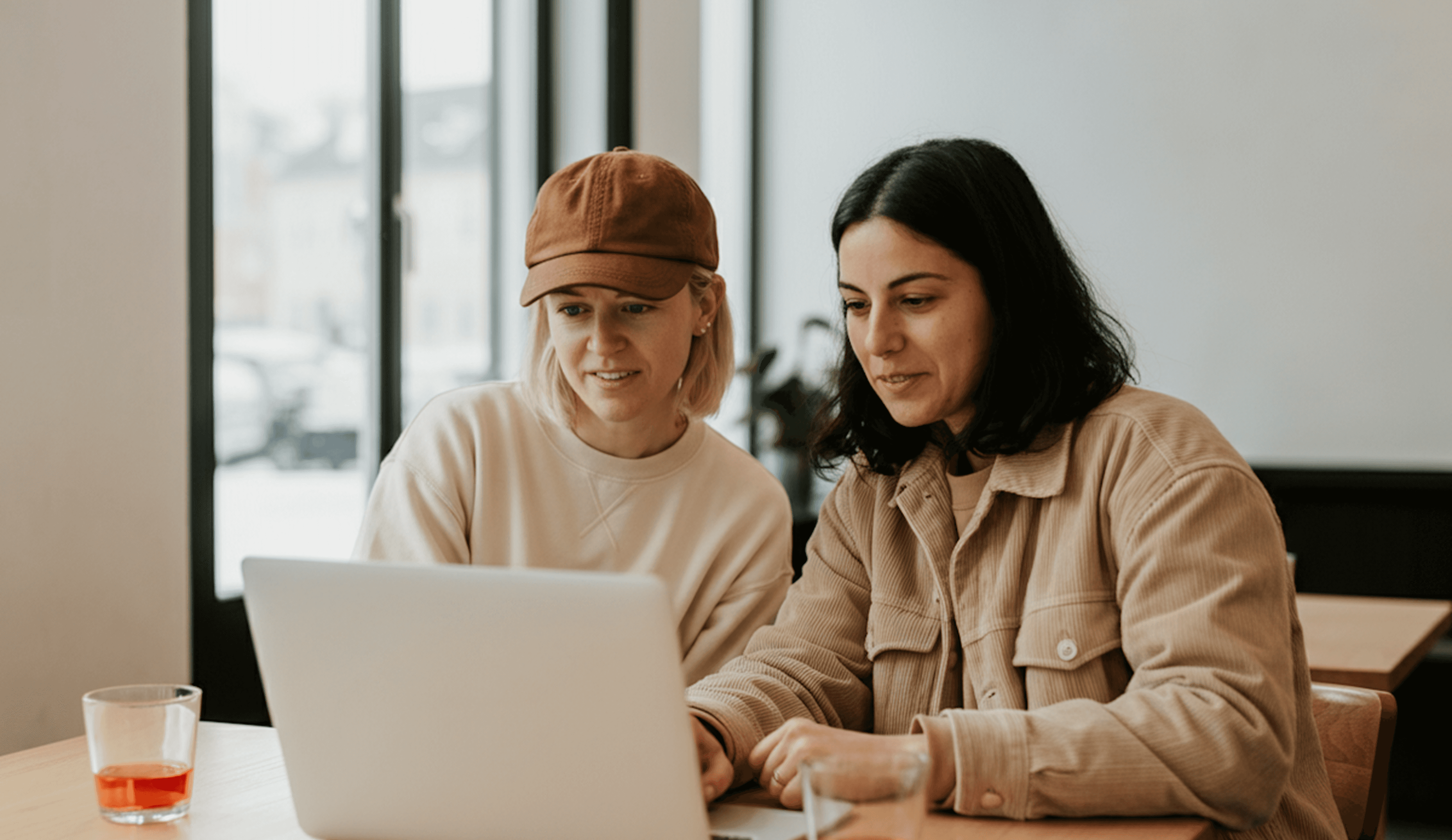 Confident two female professional using a laptop at a bright workspace with a coffee cup