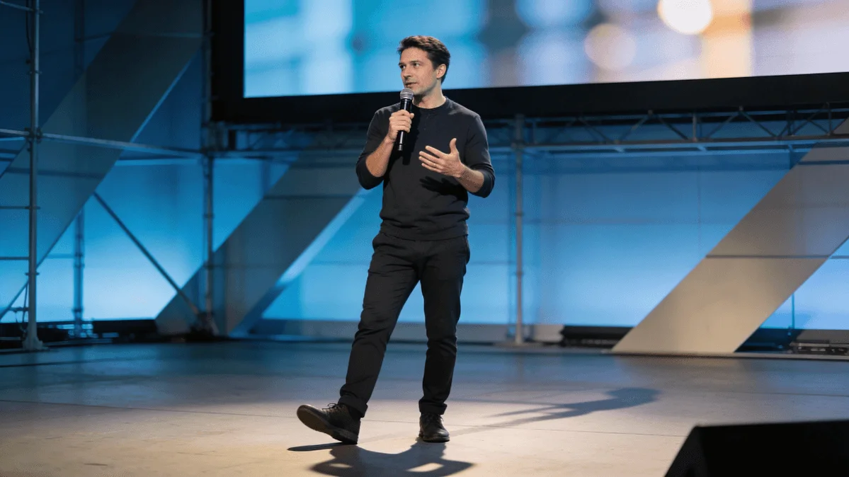 A speaker presenting at an AI conference in front of an audience, discussing real-world approaches to building AI products.