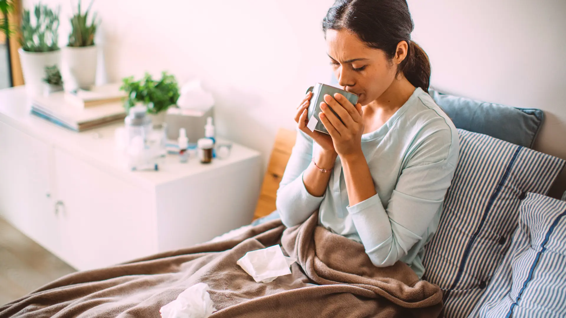 Femme malade allongée dans son lit buvant une tasse de thé chaude,