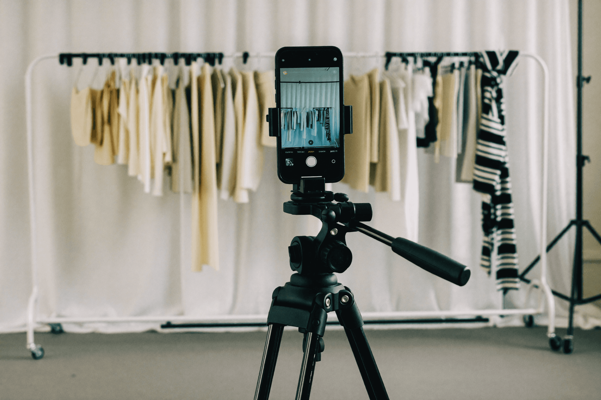 A smiling couple takes a selfie under a clear blue sky. The woman wears a red jacket, and the man, in a green top, holds a smartphone.