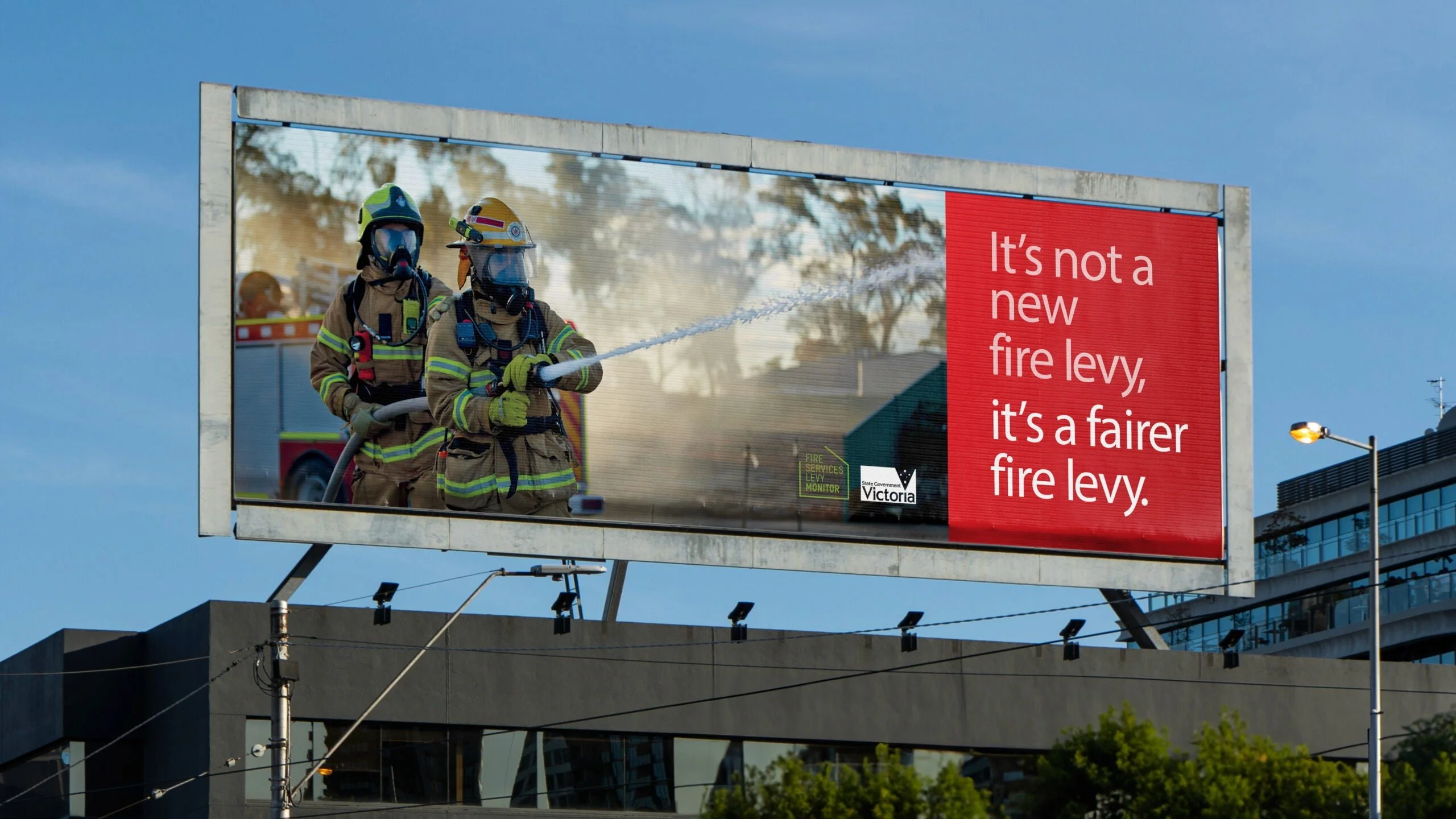 Billboard 'It's not a new fire levy, it's a fairer fire levy.' beside two firefighters with a hose, Victoria logo