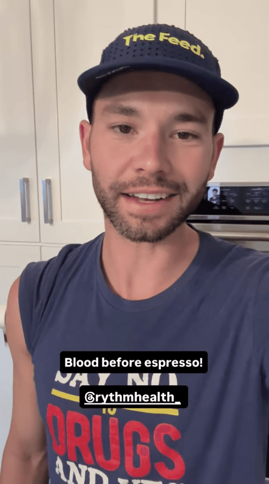 Man speaking to camera indoors with text overlay “Blood before espresso! @rythmhealth.”
