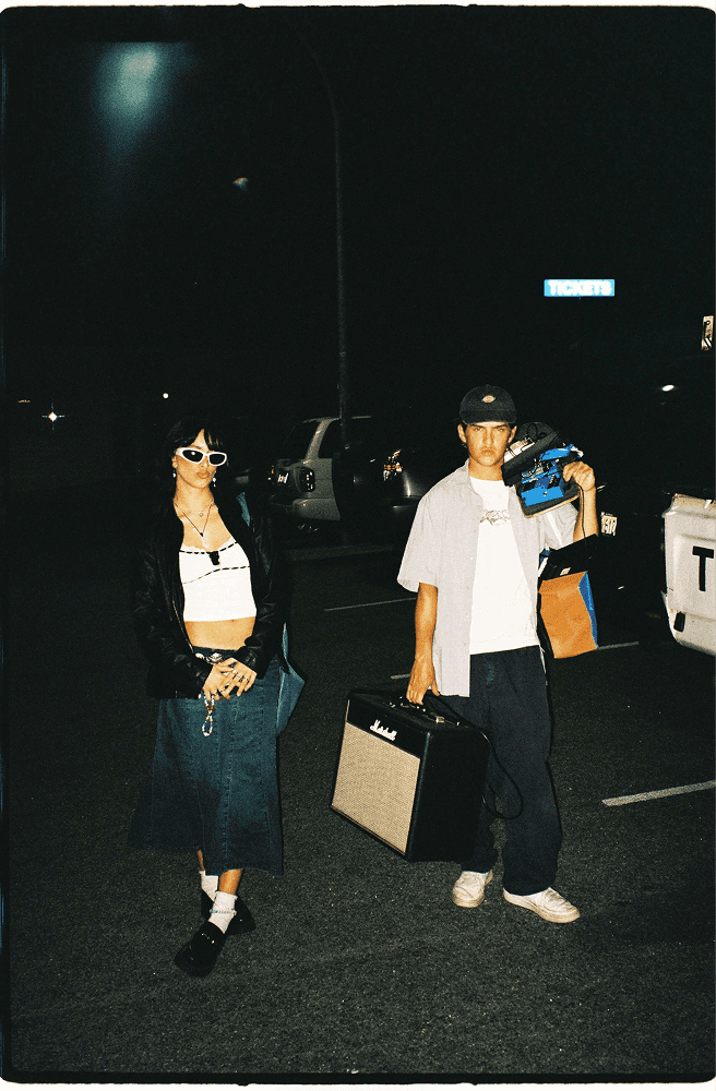 a young man and woman walking through a parking lot at night holding musical instruments