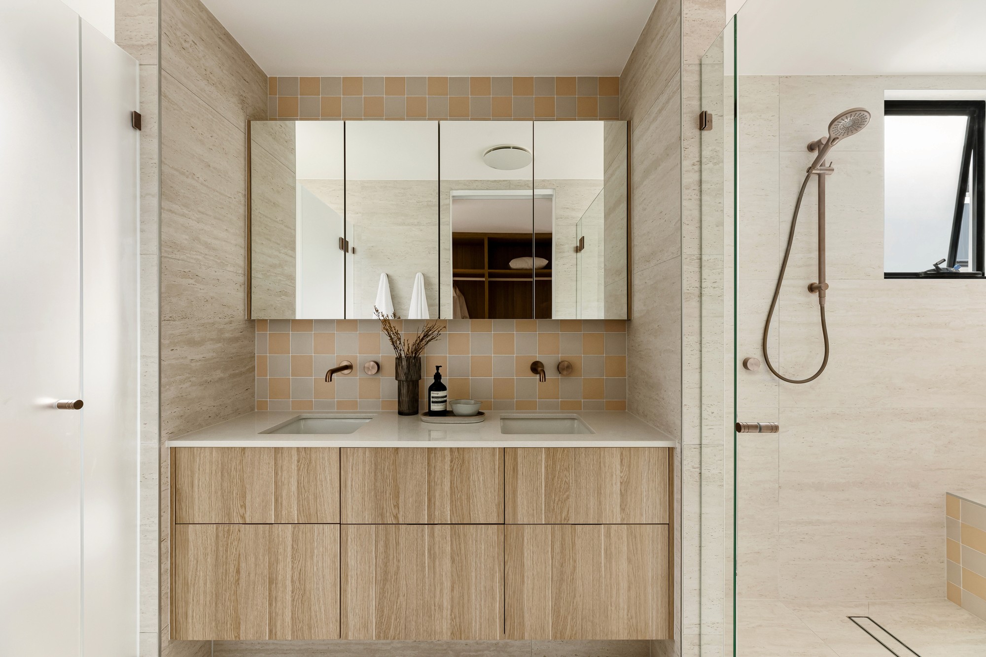 Double vanity in the ensuite with mirrored storage cupboards, warm tiles and brushed metal fittings.