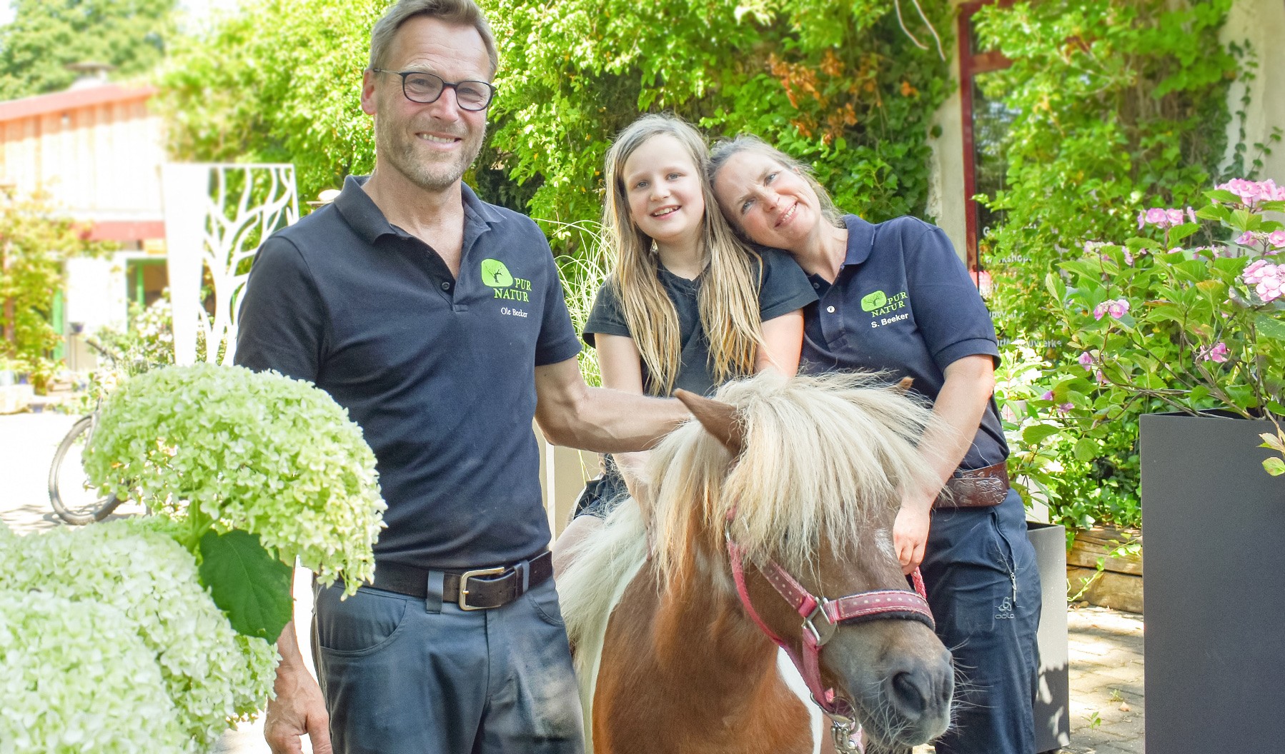 Familie Beeker von Pur Natur – Die Gartenschule in Uelzen-Veerßen mit ihrer Tochter auf einem Pony vor dem begrünten Gartencafé