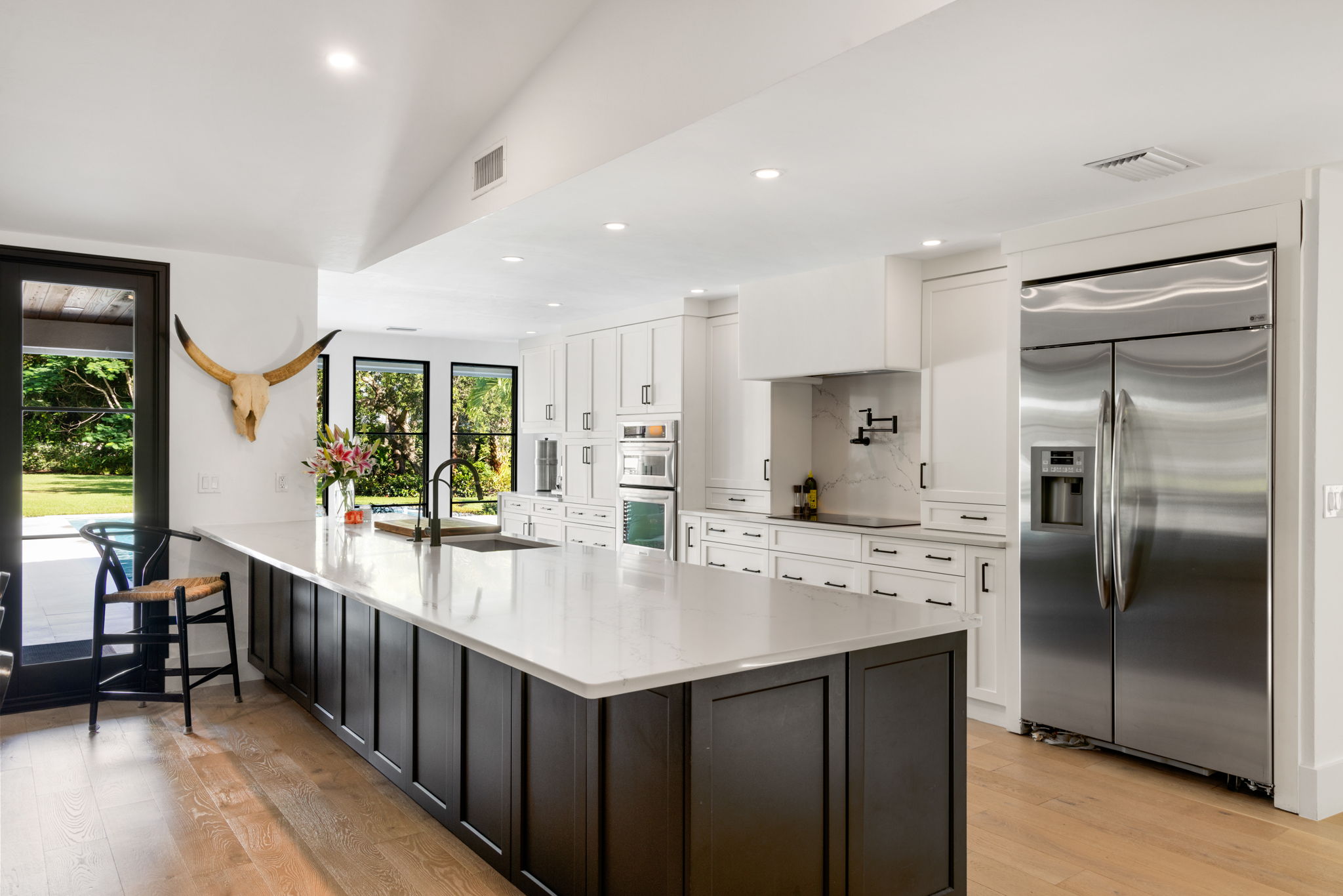 a large kitchen with white countertops and dark cabinets with a reflective fridge built in