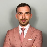 Portrait of a woman with blonde hair in a bun, light denim shirt, smiling.