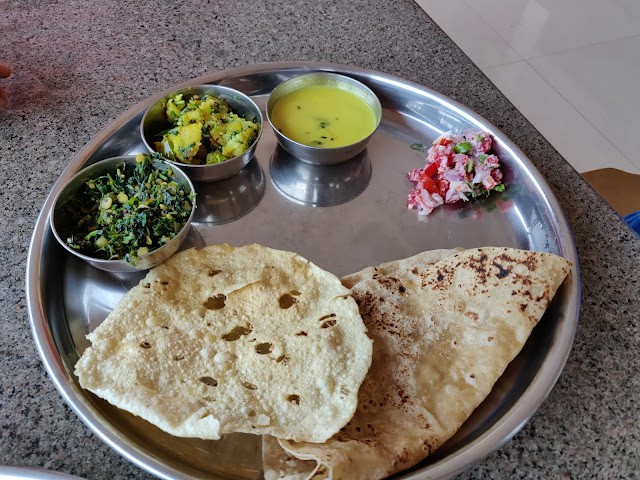 Food served in a steel thali. Numerous vaatis of vegetables, dal along with salad is served with chapatis.