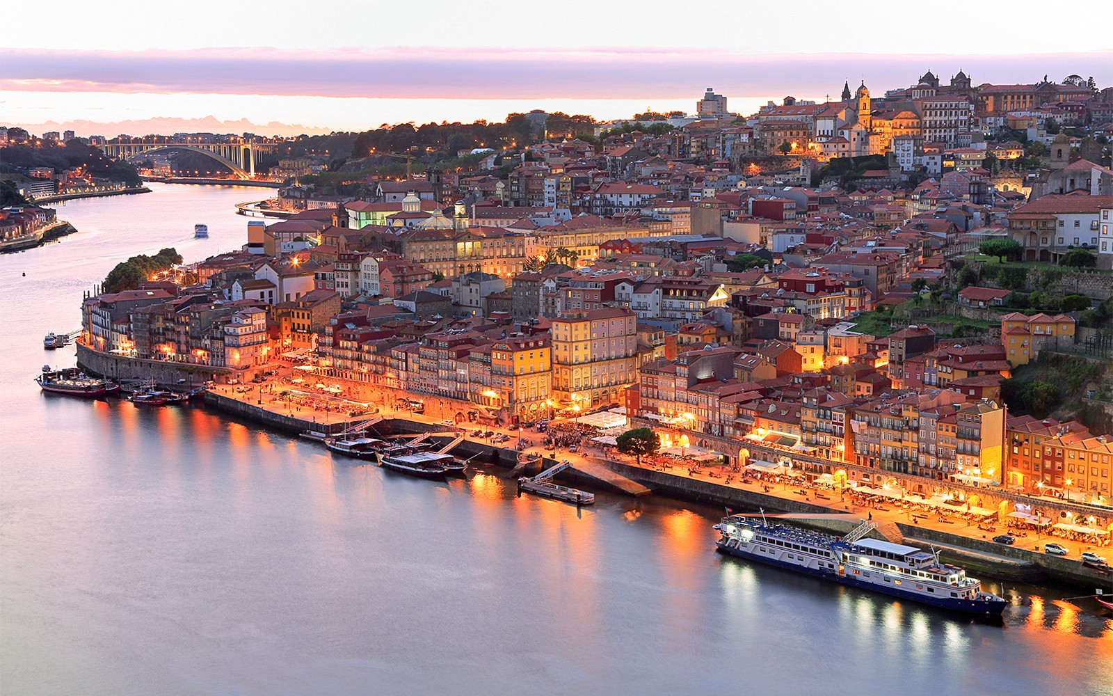 O horizonte do Porto e o rio Douro ao pôr do sol com edifícios iluminados.