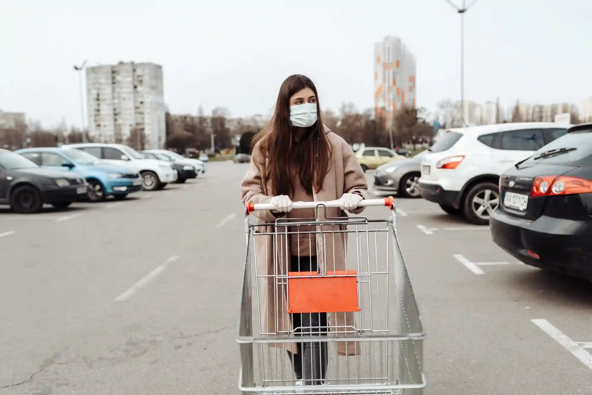 Woman in a face mask pushing a shopping cart in a parking lot.