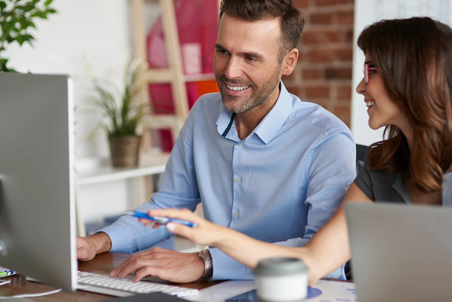 Colleagues enjoying teamwork and collaborating at a computer in a friendly office setting.