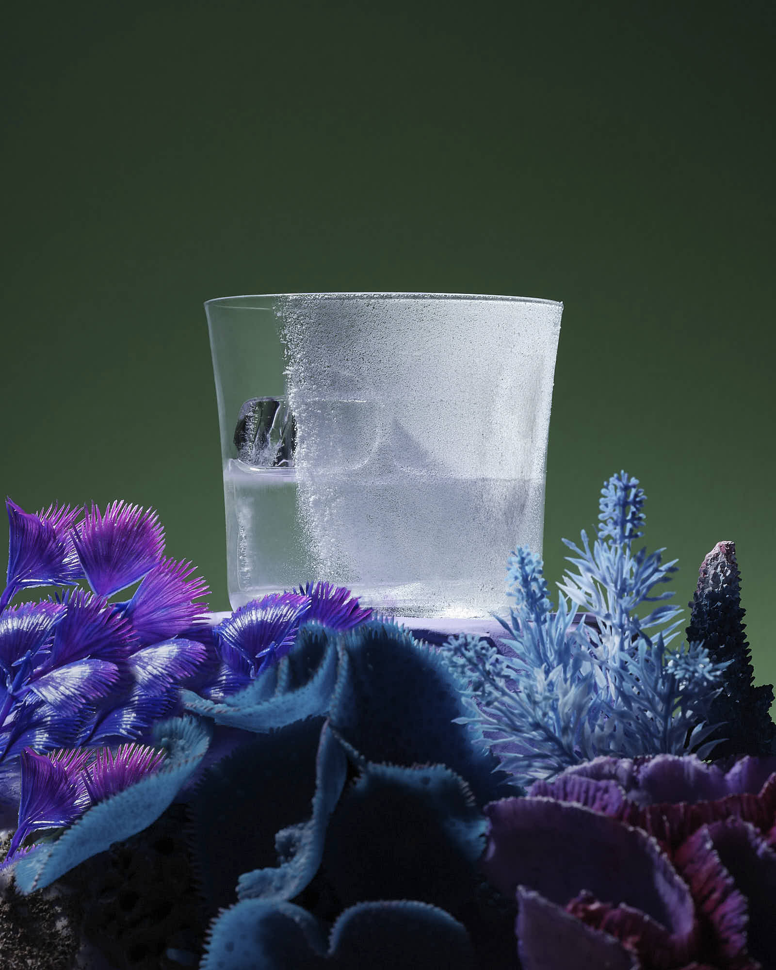 A clear glass sits atop a vibrant arrangement of blue and purple crystals against a dark green background.