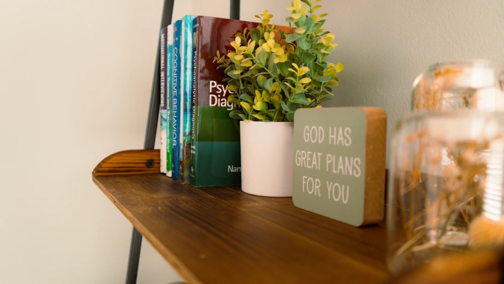 Wooden shelf with books, potted plant, and a decorative sign reading ‘God has great plans for you.'
