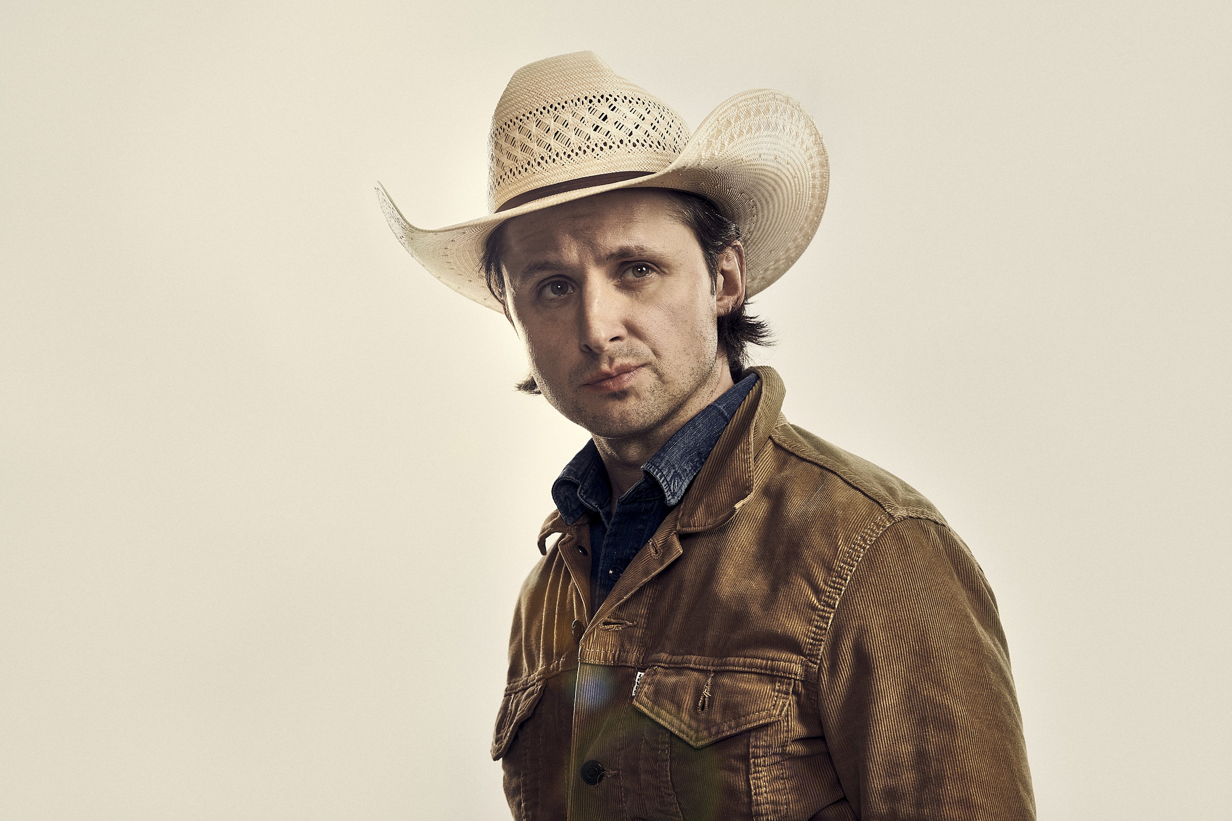 A high key and natural character portrait of a blue collar rancher. The photograph is in the style of film and television key art, publicity images. Shot in the studio in New Orleans, Louisiana. The lighting is technical and bright with a dynamic sun flair from behind the character who is portrayed by actor T.C. matherne.