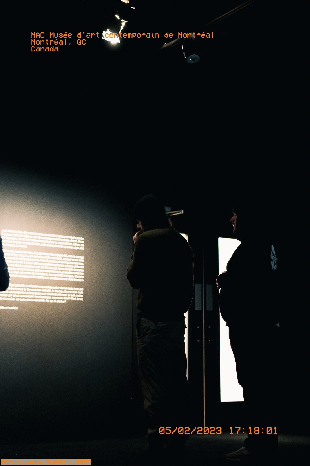Silhouettes de deux personnes devant un texte explicatif au Musée d'art contemporain de Montréal.dans le MAC