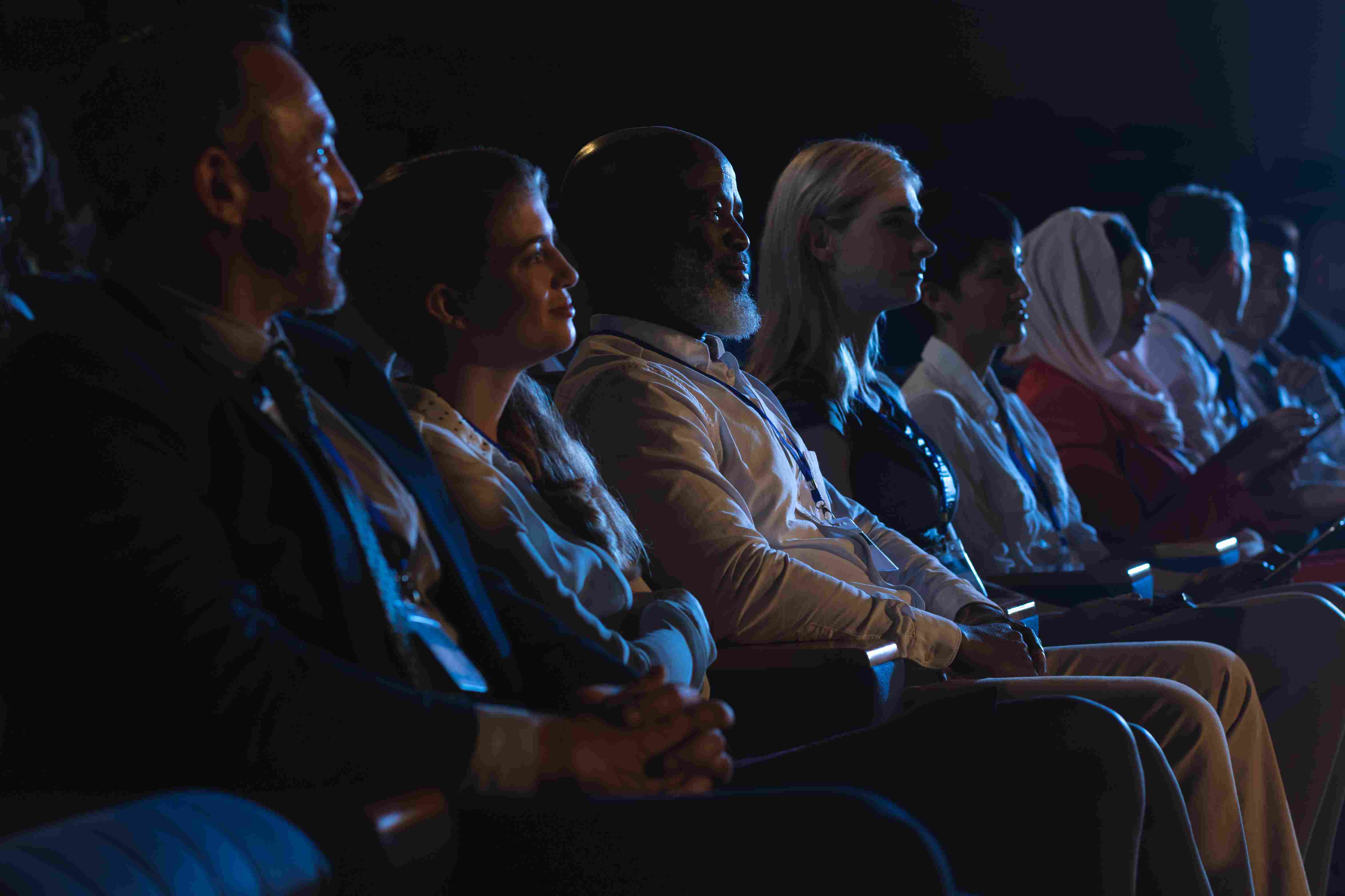 Diverse audience attentively watching a hybrid event streaming presentation in a dimly lit hall