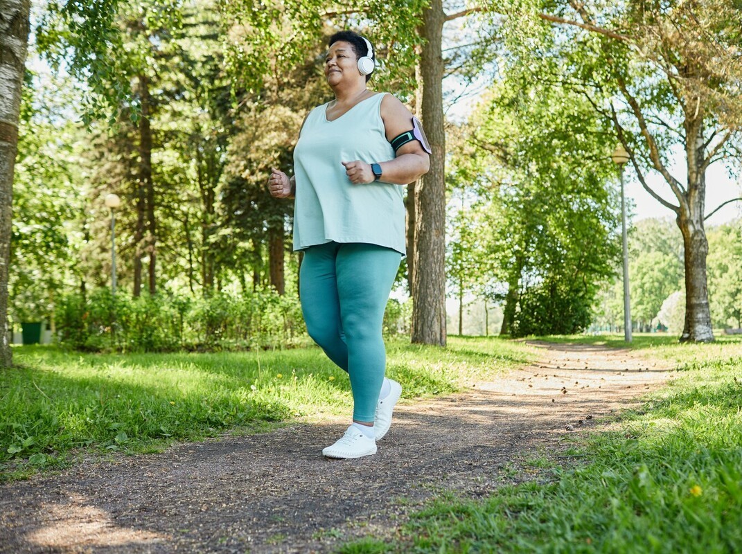 plus-sized woman walking for weight loss down a forest path with headphones