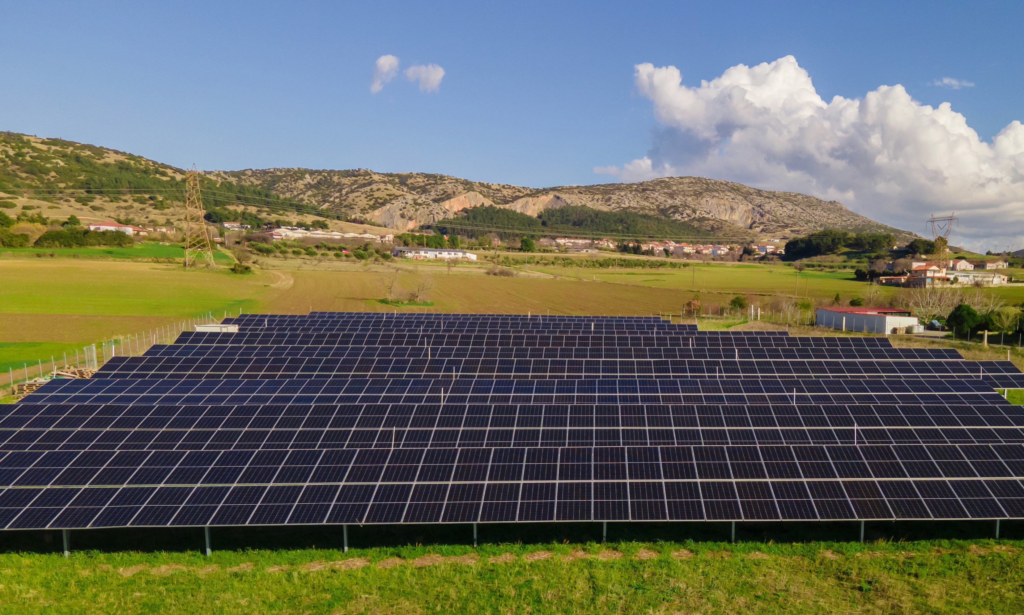 Large-scale ground-mounted photovoltaic solar array installed in rural landscape with mountainous backdrop