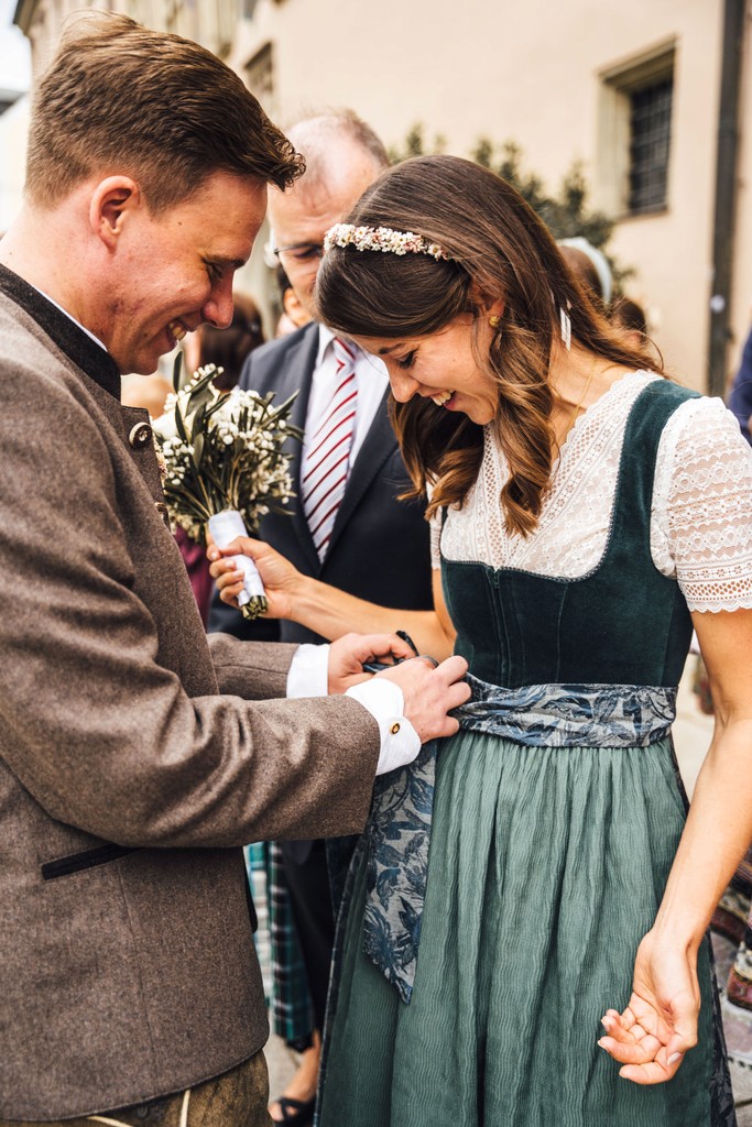 Bräutigam bindet der Braut im Dirndl erstmals die Schleife bei Hochzeit in Passau