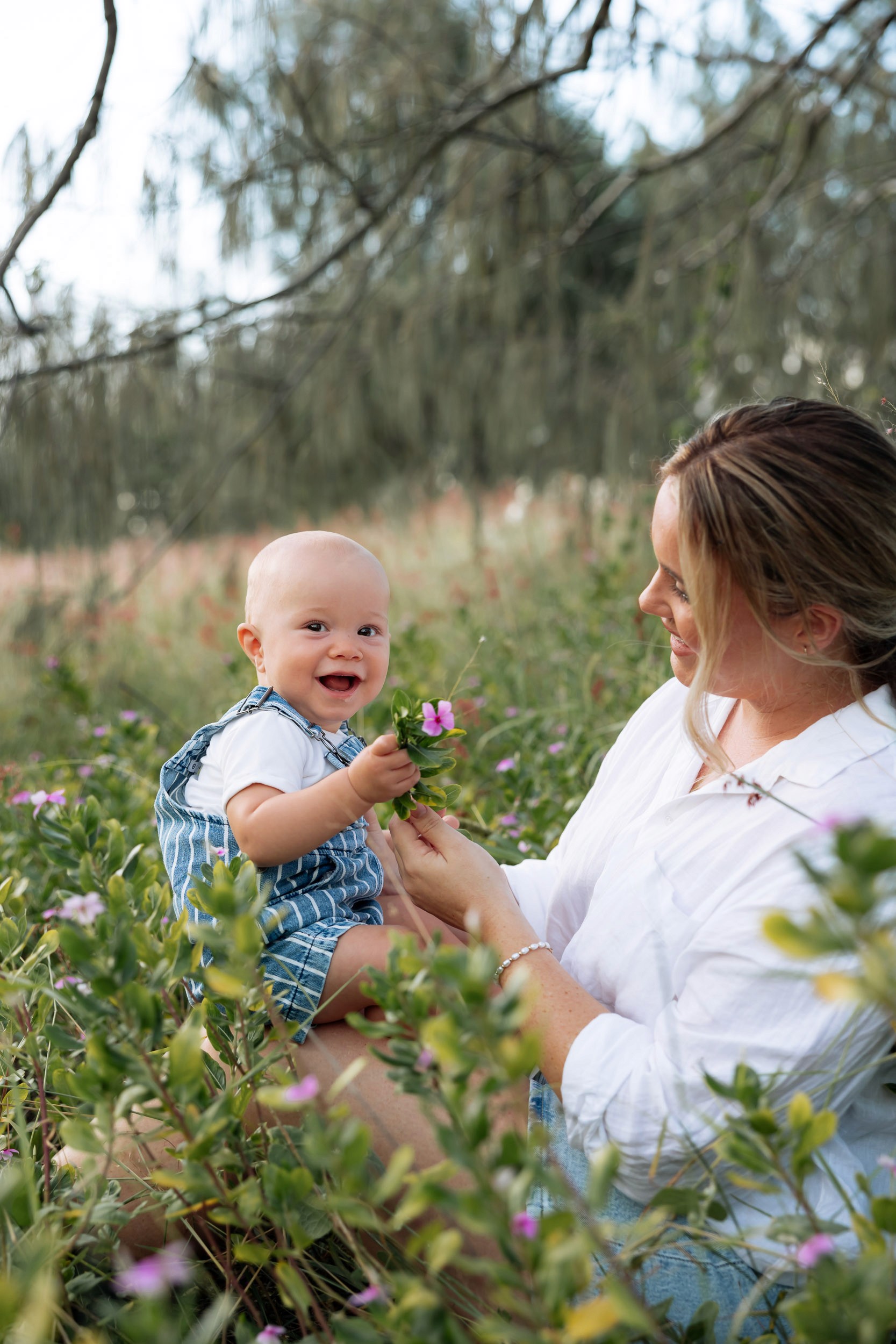 Candid portrait of mum cuddling her baby in a grassy field at sunset, natural light family photography in Mackay