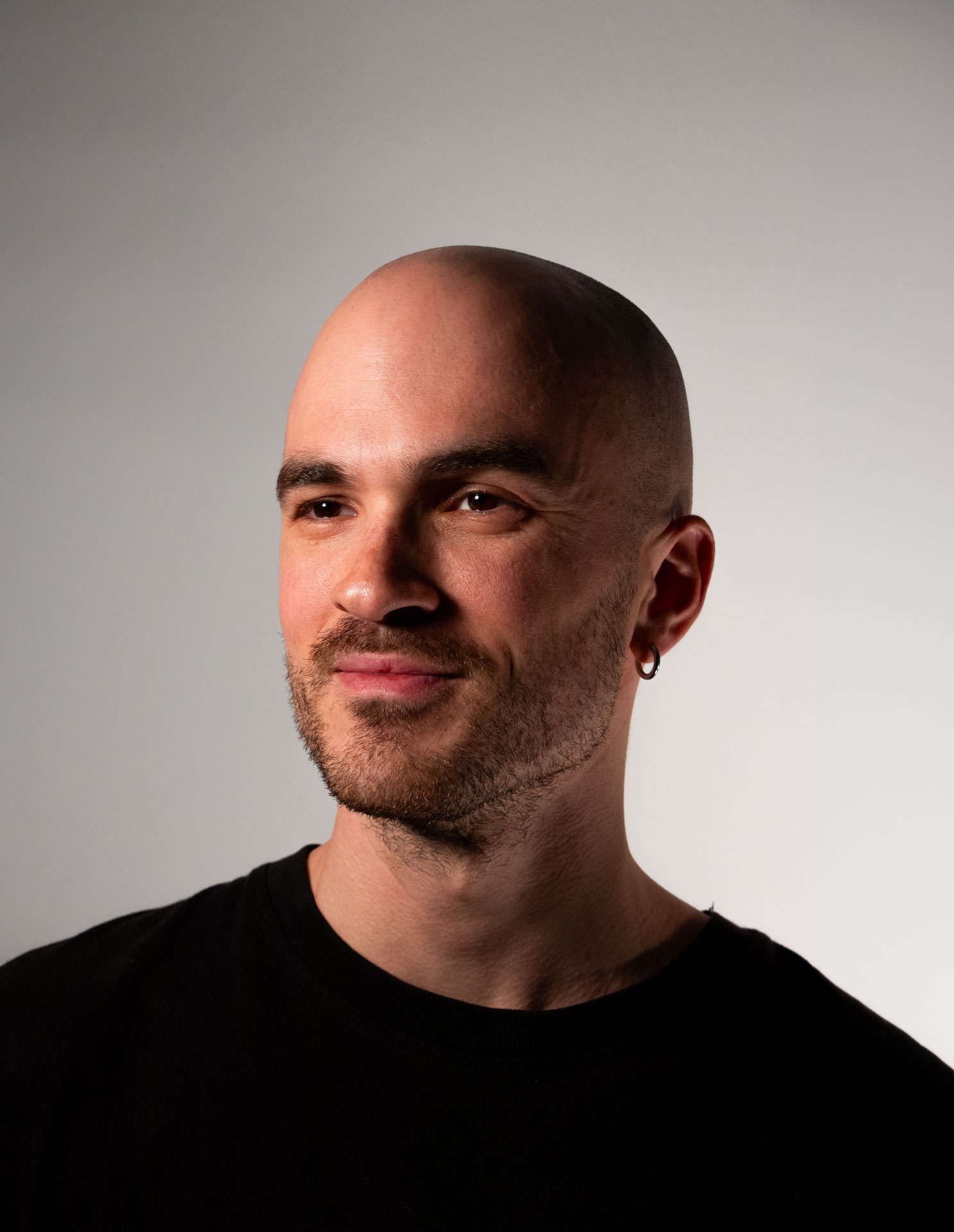 Bald man in a turtleneck, half-lit in black and white.