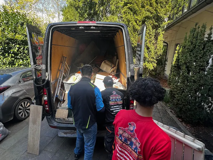 Team lädt Bauholz und Sperrgut in den Transporter vor einem Wohnhaus