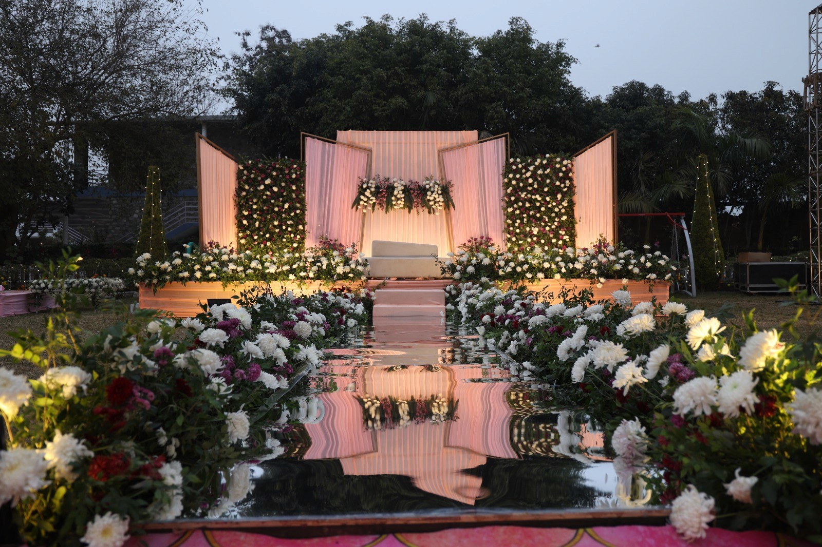 A serene outdoor wedding setup with white chairs arranged on green grass under a canopy of trees.