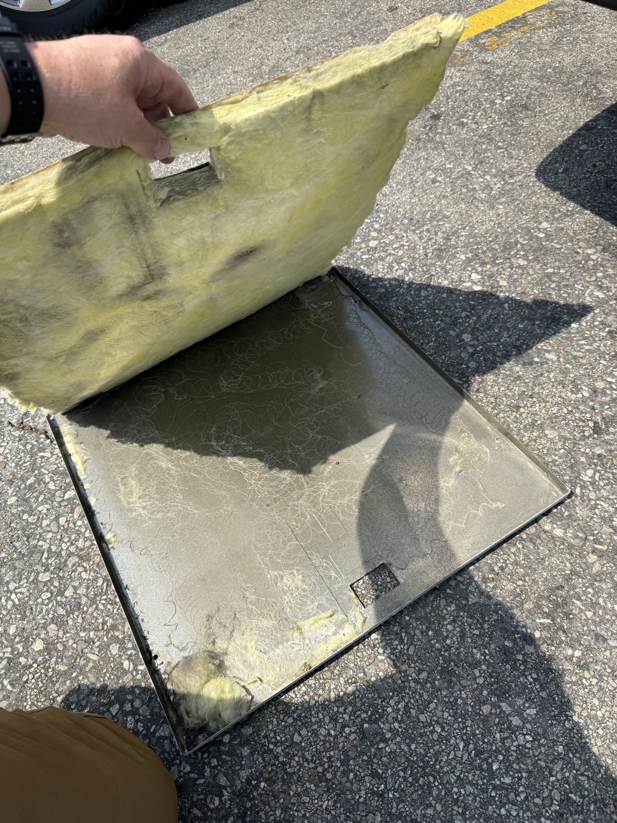 Hand pulling loose fiberglass insulation from a commercial air handler access panel.