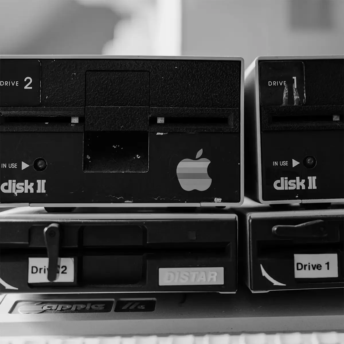Black and white close-up of vintage computer disk drives with an Apple logo, suggesting legacy, consistency, and brand recognition over time.