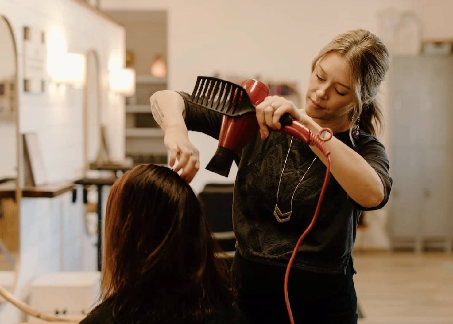 A stylist is doing a client's hair at the Camelia beauty salon. In one hand, they hold a hairdryer, and with the other hand, they adjust the hair.